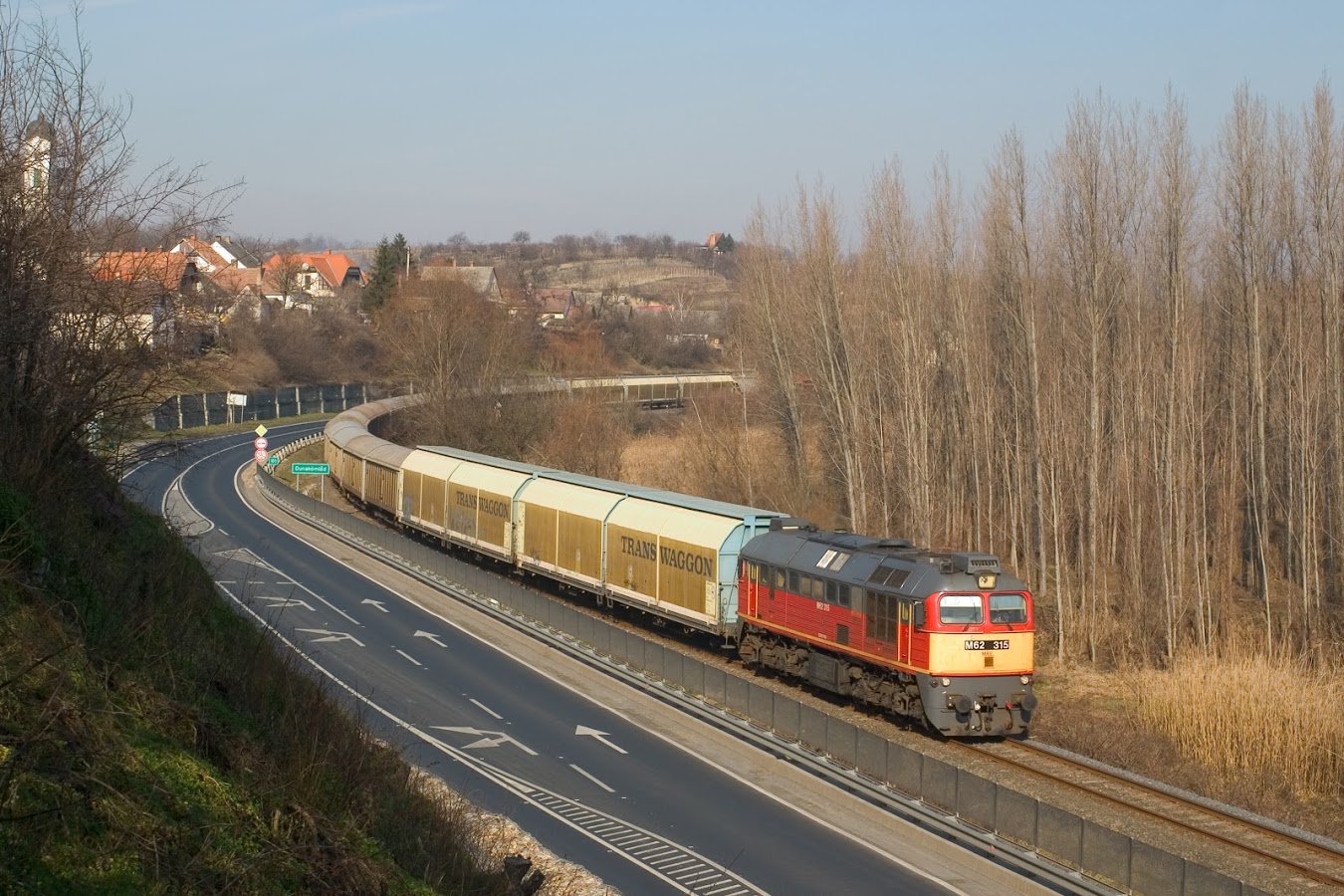 A még újszerű 315-ös Szergej húzza irdatlan vonatát Dunakömlődnél Paks felé. A szivacsnak való kocsikat látjuk, de a fák mögött mégegyszer ennyi gabonás kocsi is a menettel tart. A képre kattintva galéria nyílik Vörös Attila fotóiból