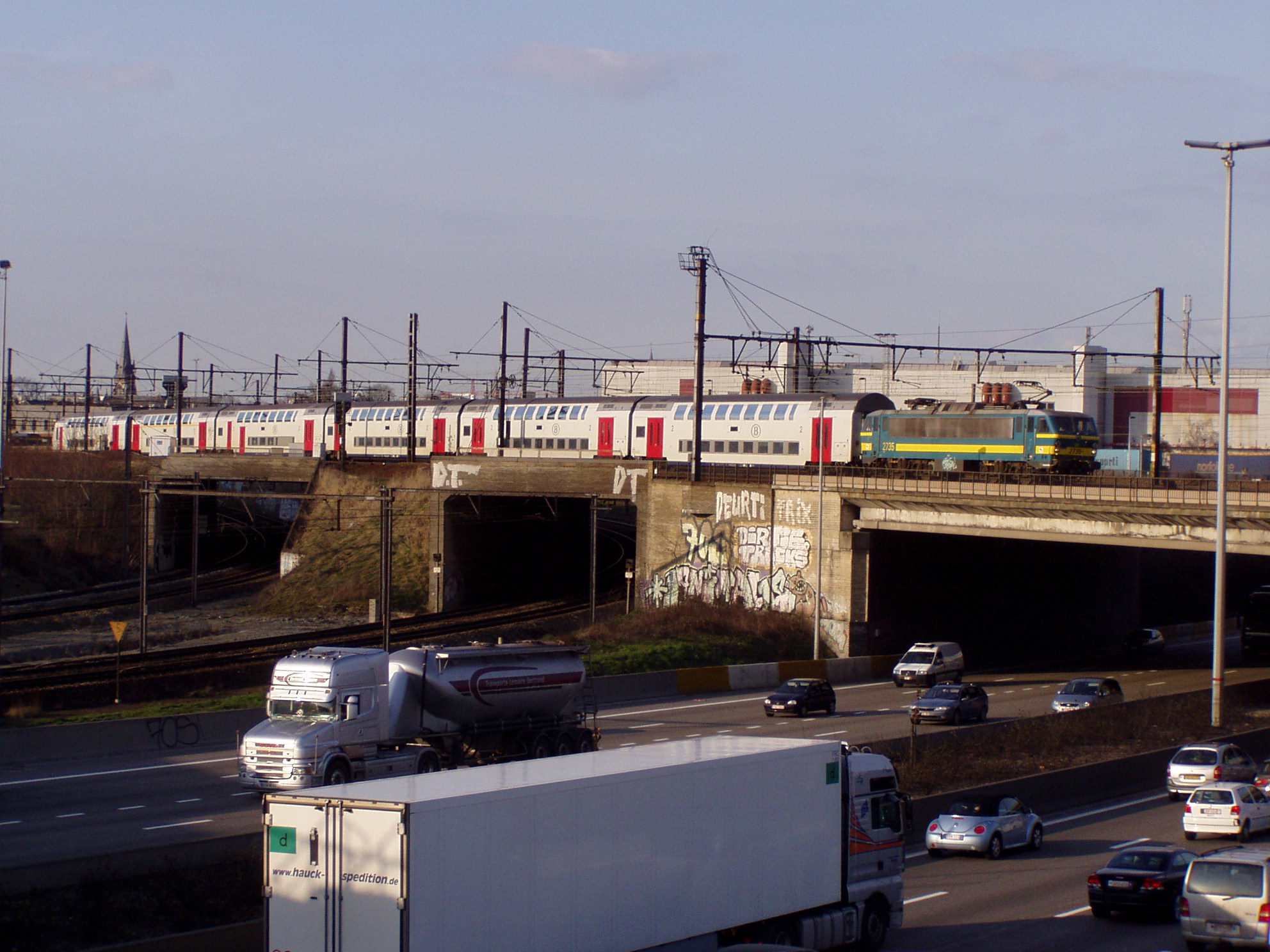 Egy Brüsszelen át Charleroi-ba tartó emeletes intercity halad át az autópálya-gyűrű fölötti hídon. A képen jól látszik a négy, nyugatra tartó elkanyarodó vágány