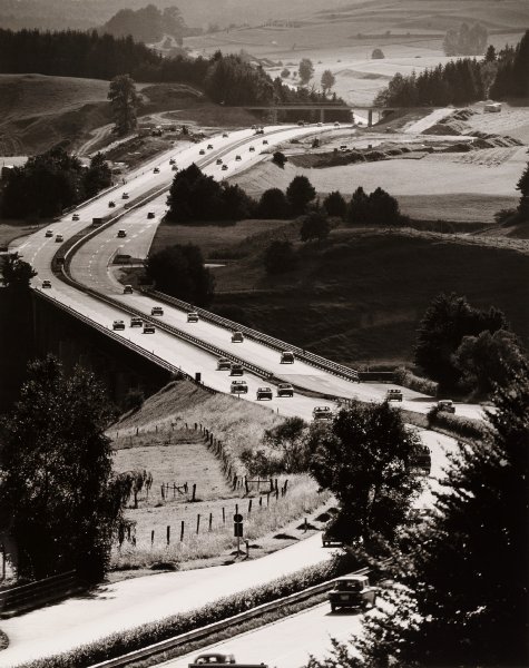 Peter Keetman fotója 1967-ből az A8-as autópályát ábrázolja a bajorországi Bergen mellett. Feltűnő a szelíden csordogáló forgalom, gondos kezek az útpadka mellett szénakupacokat képeztek. A leállósáv nélküli kialakítás már nem ugraná meg a magyar szabványt sem, az ívek és a hosszszelvény is gyanús