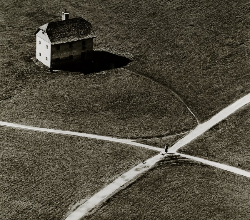 Toni Schneider fényképe egy ház és egy útkereszteződés viszonyát egy akkor forradalmian új látószögből mutatja be. Ma, a drónfotók korában a látószög nem, a kompozíció tökéletessége viszont lázba hozhat. Az út itt nem közlekedési nyomvonal, egyszerűen kompozíciós elemmé válik