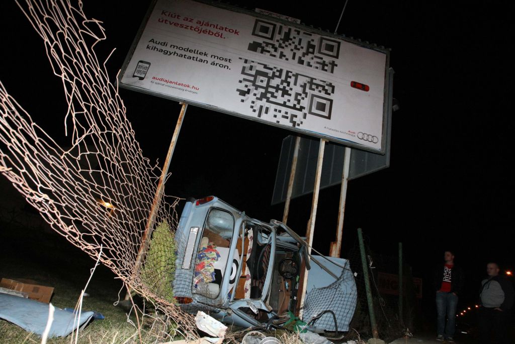 Óriás reklámtábla tartóoszlopai között összeroncsolódott és oldalára borult Trabant vár elszállításra<br />(fotó: Bugány János-MTI)
