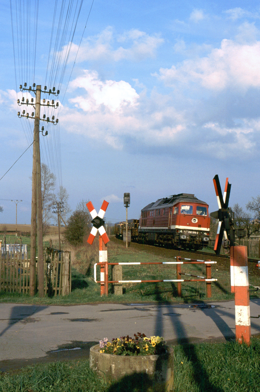 Acéláruval rakott vonattal robog át a még a DR-időket idéző festésű 232 570-es Oberwellenborn közelében egy útátjáron 2002. április 19-én. A képre kattintva galéria nyílik (fotó: Indóház-archív | Jörg Boeisen)