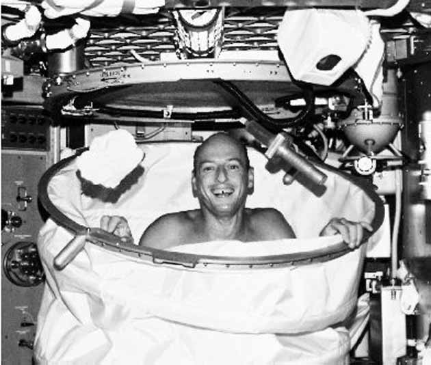 Régi űrállomás, fekete-fehérben: a Skylab asztronautája vigyorog egy forró fürdő után az összecsukható, szigetelt zuhanykabinban. Csak 3 gallon vizet használhat egyszerre.