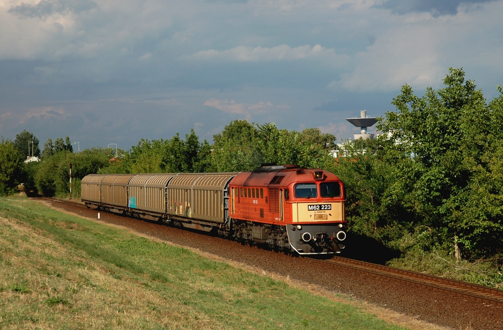 Négy eltolható oldalfalú kocsival halad a 77027. számú tolatós tehervonattal Szeged-Rendező felé a 223-as Szergej. A háttérben a rókusi víztorony látható