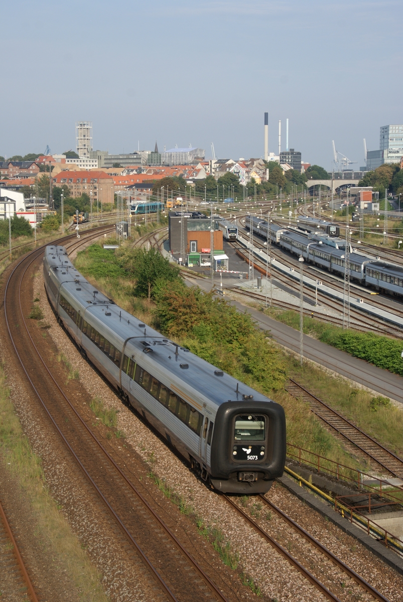 Gumiorrú IC3-as motorvonat gyorsít Aarhus pályaudvarának tárolóvágányai mellett