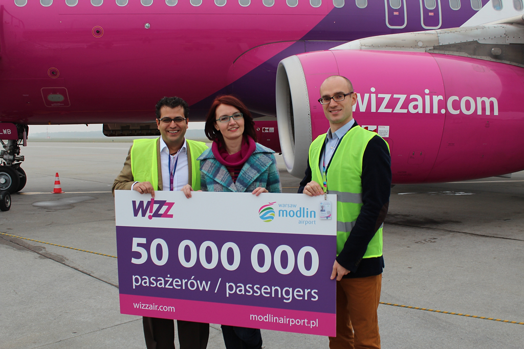 Daniel De Carvalho a Wizz Air vállalati kommunikációs menedzsere és Piotr Lenarczyk a varsói Modlin repülőtér vezető értékesítési szakembere gratulál a szerencsés utasnak, Anna Wilsonnak<br>(forrás: Wizz Air)