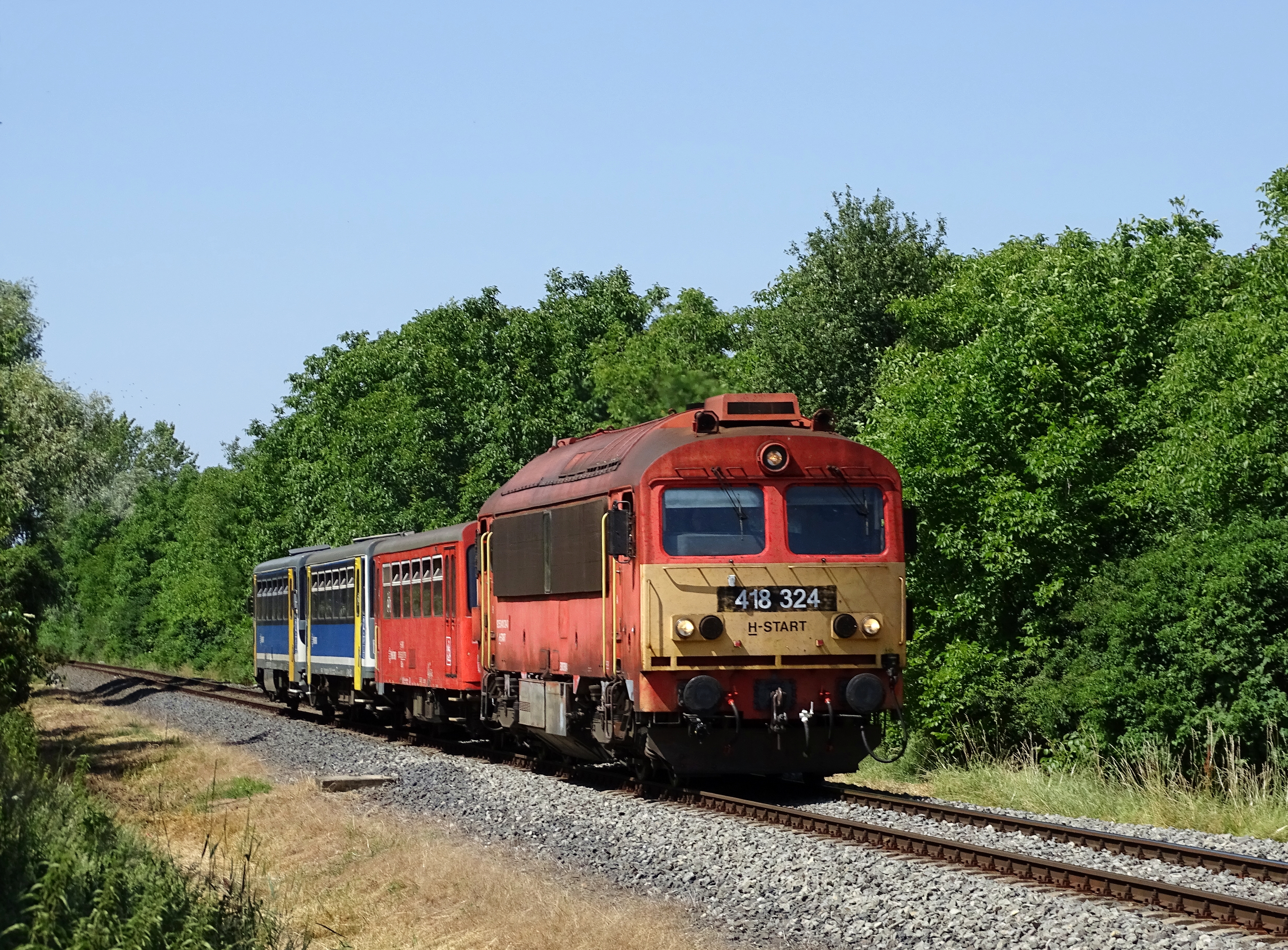  A tavalyi nyári menetrend tartogatott néhány kellemes fotótémát, hiszen vasárnaponként ismét előfogatokkal közlekedett a 19773-as füredi személy, a 19776-os tapolcai vonat pedig Vikinggel az élen jeleskedett. Németh Gábor 2025. június 22-én készült felvételén a 19773-as porol Kisapáti közelében, a dízelgép a 19706-os Hullámra kellett