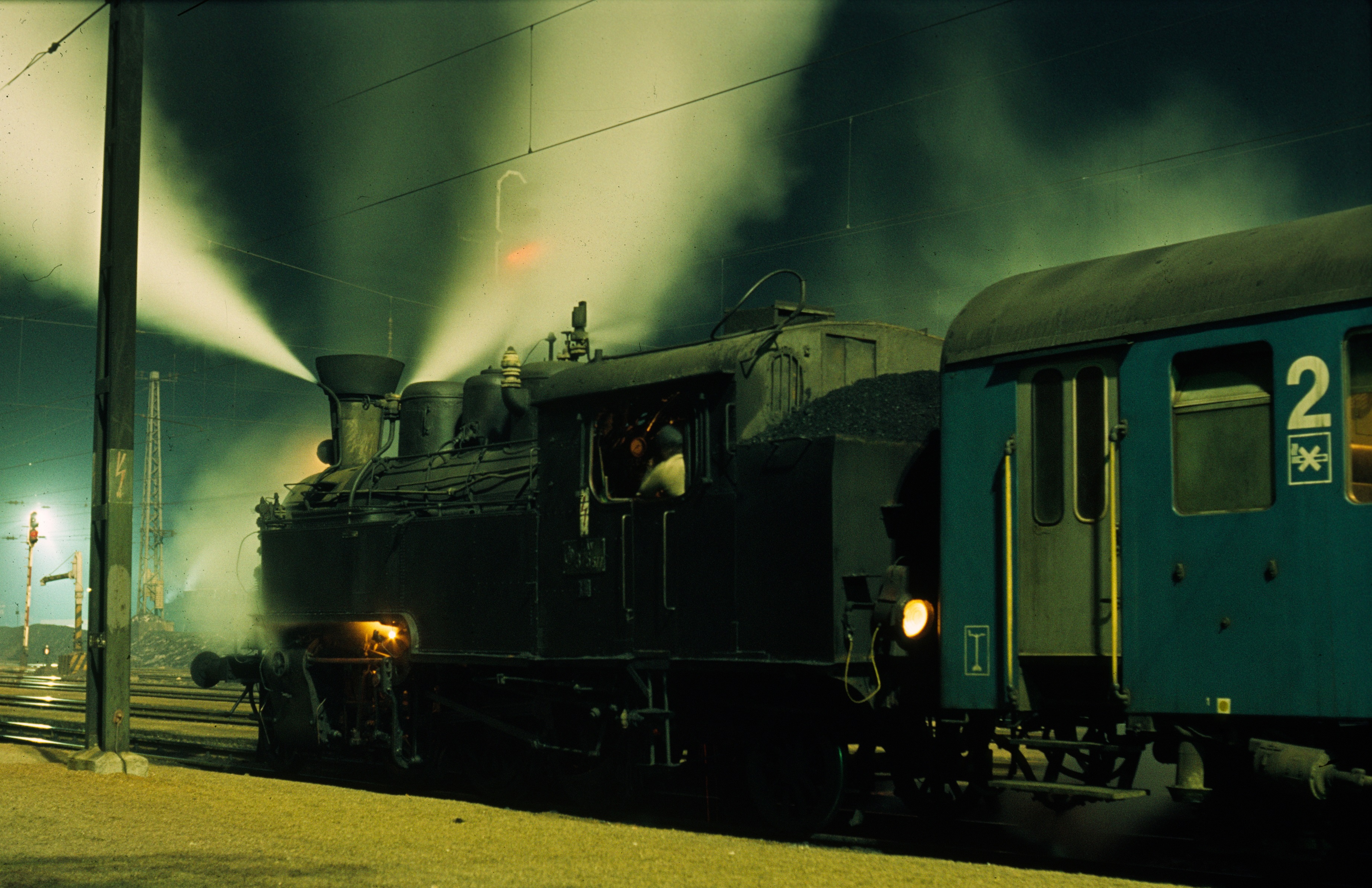 Éjjeli fények játéka Szerencs állomáson 1982. március 27-én. A 375,527-es pályaszámú gőzmozdony a legnagyobb észak-magyarországi, 375-ös bázison áll indulásra készen személyvonatával. A masina összes lámpáját felkapcsolták. A bal oldali gőzfelhő a légsűrítőből, a jobb oldali a turbódinamóból származik (fotó: Mező András)