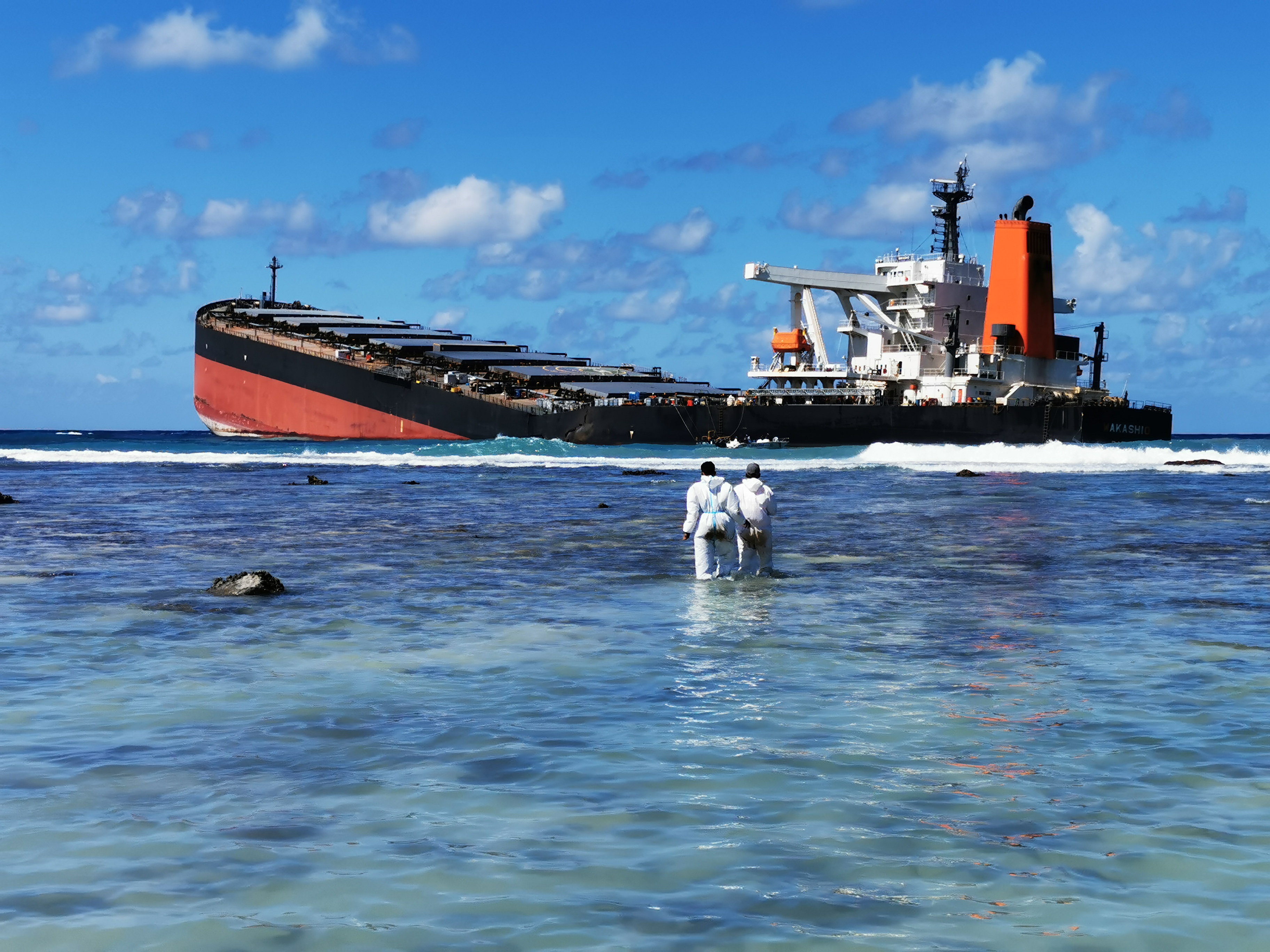 Védőruhás mentőmunkások állnak a hullámokban az MV Wakashio roncsa közelében, 2020. augusztus 13-án