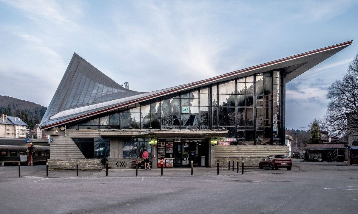 Predeal, felvételi épület 1030 méter tengerszint feletti magasságban.. Az 1969-ből származó alkotás a romániai, hegyvidéki üdülőhelyekre jellemző plasztikus kifejezésmóddal igyekszik kihangsúlyozni az épület funkcióját. Az építmény egy hiperbolikus paraboloidot sejtet, élei egy rombusz alakú részt fednek le, miközben az utascsarnok ablakzata széles panorámát nyit a környező hegyekre. A Băile Olăneşti állomáson megépülttől eltekintve ez Románia egyetlen nyereg alakú, geometrikus formákról árulkodó felvételi épülete. (És lásd még a szántódi rév utasváróját…) A felvételi épület lassan enyészik, egyes helyiségek, például a kávézó vagy a várótermek egy része zárva vannak. Körülötte azonban parazita pavilonok jelentek meg, ezekben többek között hot-dog, üdítő és snack kapható (fotó: romd.socialistmodernism.com)